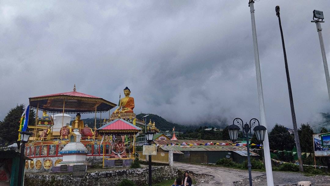 Golden Buddha statues at Tawang Monastery beneath a cloudy Himalayan sky