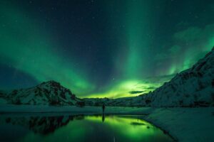 Green aurora borealis glowing over a snow-covered mountain landscape in the Arctic