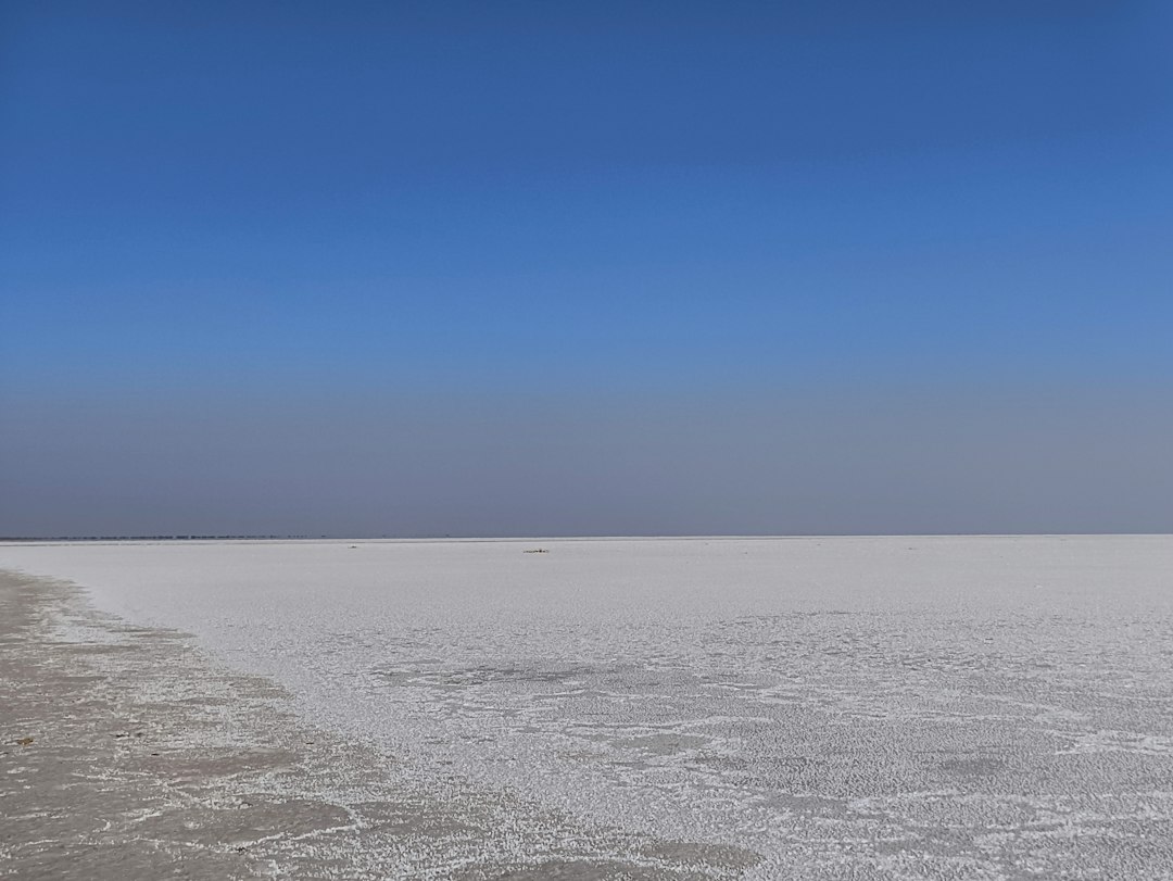 The vast white salt flat of the Rann of Kutch under a clear blue sky, host to the Rann Utsav tent city